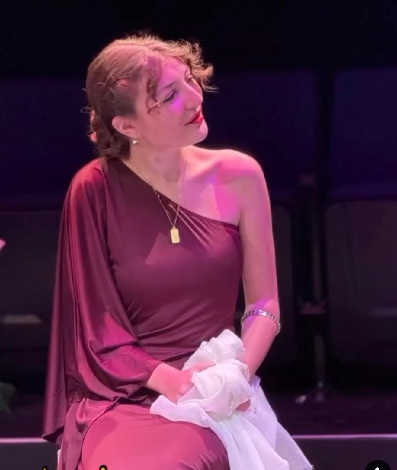 Savannah Lynn in a burgundy gown seated under stage spotlight