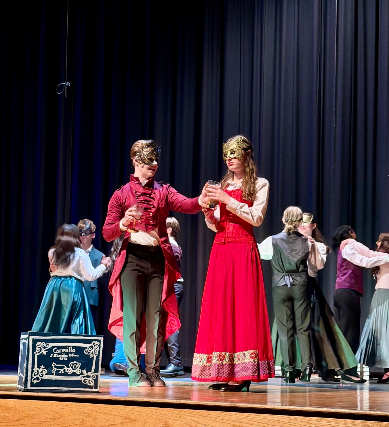 Savannah Lynn in a red period gown at a masquerade ball scene on stage