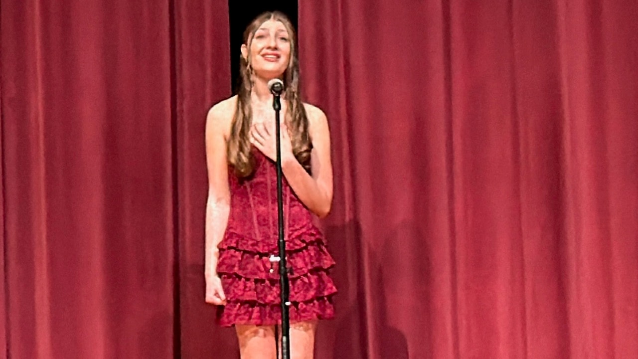 Savannah Lynn performing a solo vocal number at a microphone in a red dress