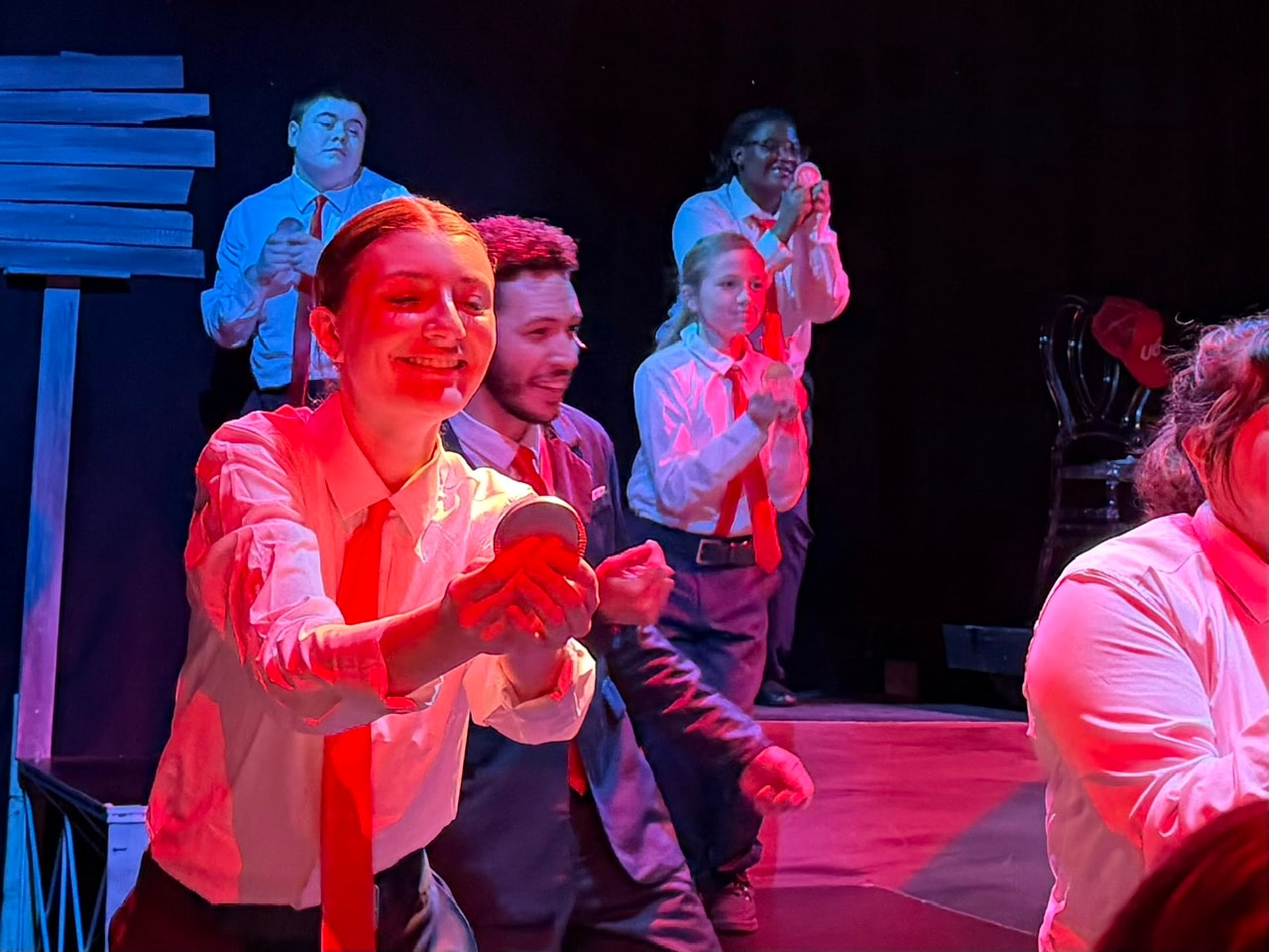 Savannah Lynn performing in Urinetown ensemble under red stage lighting
